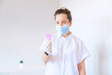 Female Gynecologist doctor with shocked face expession looking at pink period cup on white backdrop. Mentrual cup, zero waste, eco friendly. Replacement of absorbents