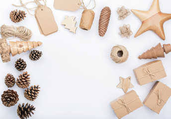 Festive Christmas frame background in the shades of brown on white table. Top view of gift boxes, various accessories, wooden decorations, pinecones, tags, copy space, selective focus