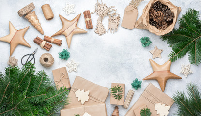 Christmas frame background. Top view of fir tree branhes, brown gift boxes, various accessories for handmade presents, wooden decorations pinecones, tags on white table, copy space, selective focus