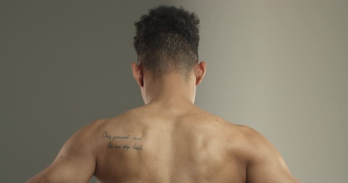 Close-up rear view of dark-skinned sportsman back, athlete flex biceps on arms, showing muscles. Bodybuilder show-off physical form, strong man after workout in gym, concept of sports and body