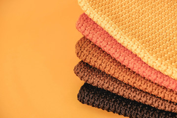 Stack of knitted material from threads of yellow, orange, brown colors on a orange background. Top view. Copy, empty space for text