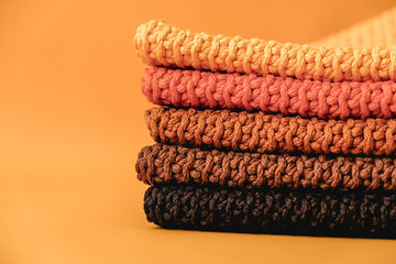 Stack of knitted material from threads of yellow, orange, brown colors on a orange background. Copy, empty space for text