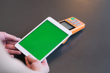 over shoulder view of man holding green screen digital tablet over pos terminal on counter. blur background