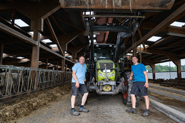 Lanwirtschaftliche Familienbetriebe, Landwirt mit seinem Sohn im Rinderstall vor einem Traktor. © Countrypixel