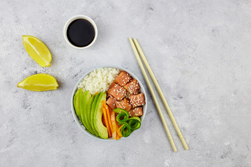 Hawaiian dish poke bowl with salmon, cucumber, avocado on grey background. Top view with copy space.