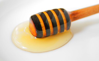 
honey dipper with natural liquid honey on a white plate.