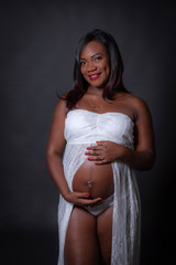Mujer negra embarazada en estudio con vestido blanco
