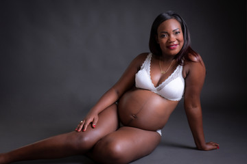 Obraz premium Mujer de raza negra embarazada en ropa interior blanca sentada