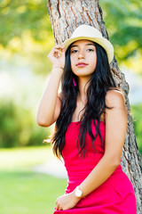 young brunette Latina girl with long black hair and black eyes, wearing a red dress and light hat, looking at the camera