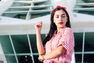 Young latin girl with black hair and red ribbon in her hair, standing looking at the camera on a sunny day with white background, wearing red striped shirt