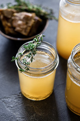 Glass jar with yellow fresh bone broth on dark gray background. Healthy low-calories food is rich in vitamins, collagen and anti-inflammatory amino acids