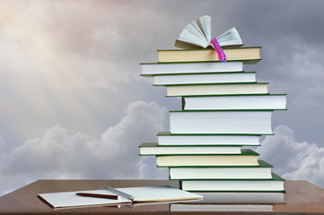 Autumn concept. Stack of books and exercise book on table against cloudy sky