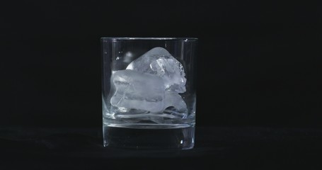 Ice cubes melt in the alcohol, whiskey glass and smoke is floating against a black background