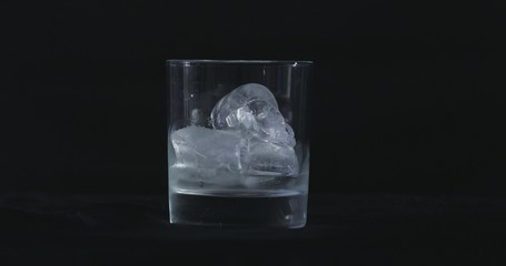Ice cubes melt in the alcohol, whiskey glass and smoke is floating against a black background