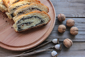 Slices of poppy seed strudel on round wooden board with whole walnuts. Top view, selective focus