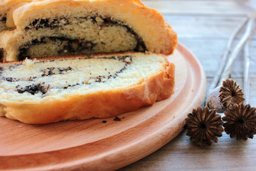 Homemade roll with poppy seeds on round wooden board background. Top view. Selective focus. Slices of cake