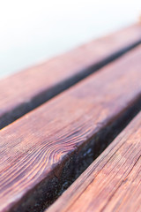 Diagonal Wooden deck of a jetty in Lake Garda. The sun is reflected in the water. The wood is warm, brown in color. Detail, macro picture with bokeh.