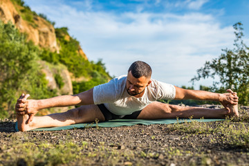 Fototapeta na wymiar Young fitness man doing yoga exercise outdoors at the quarry lake. Handsome young man with a beard doing yoga exercise.