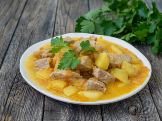 Romanian cuisine - fresh homemade meat and potatoes with parsley. Stew with pork and vegetables on a wooden background. Tasty and nourishing lunch.