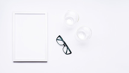 Summer composition. White wooden frame with empty space for text. Next to it are glasses and two glass mugs. Everything is arranged on a white background. Flat top view.