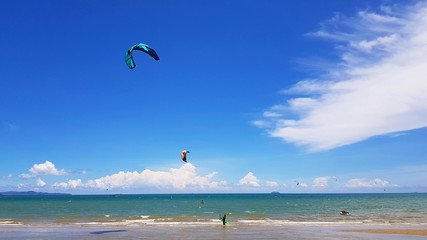 Many people or tourist playing kite surfing on sea with clear blue sky and cloud background and copy space at tropical beach, Chon ฺBuri, Thailand. Extreme activity and sport in summertime

