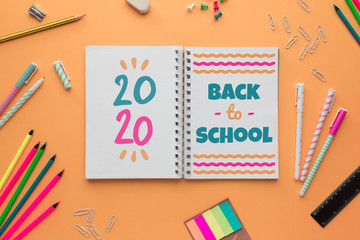 Stock photo of back to school with an open notebook with lettering and some stationery objects on a salmon background