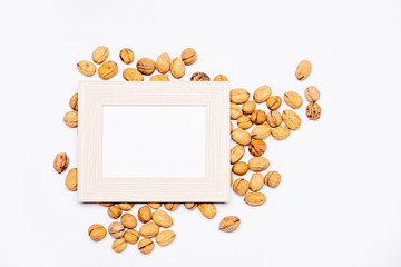 Wooden frame with an empty space for text, lying flat on loosely arranged walnuts. Everything is arranged on a bright table. Flat, top view, no people.