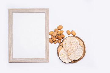 Still life of organic products. Empty wooden picture frame. Walnuts, organic rice bread stacked on a round piece of wood. Everything is placed on a bright table. Flat, top view, no people