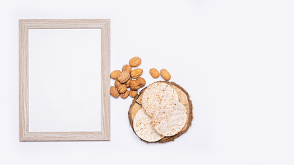 Obraz na płótnie Canvas Still life of organic products. Empty wooden picture frame. Walnuts, organic rice bread stacked on a round piece of wood. Everything is placed on a bright table. Flat, top view, no people