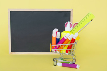 Back to school concept on yellow paper background. Basket with stationery. books. blackboard.