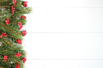 A branch of a Christmas tree with red berry decorations on a white background, located on the left side of the image. with space for text on the right
