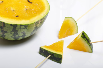 Pieces of yellow watermelon on sticks. Plate on a white surface.