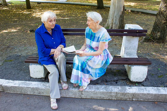 The two elderly women together in a summer park with newspaper.