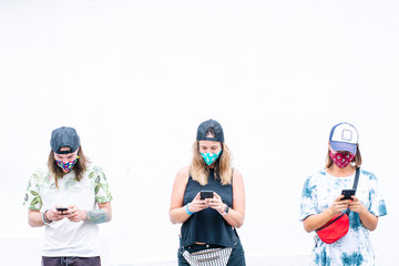 Group of friends chatting with smart phone and wearing mask outdoors
