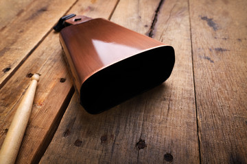 Copper Cowbell musical instrument on a wooden background with drumstick