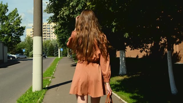 Beautiful young woman in short dress walks on the sidewalk in sunny day