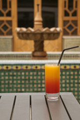 a glass of orange juice with syrup in a glass against the background of a Moroccan fountain