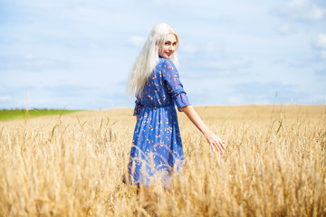 young happy blonde in a blue dress posing in a wheat field