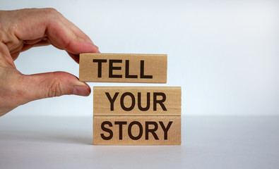 Male hand placing a block with word 'tell' on top of a blocks tower with words 'tell your story'....