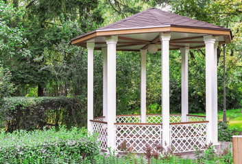 White wooden gazebo in a summer park. Garden pergola.