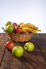 fruit basket with bananas, apples and oranges on polished wood, placed on rustic wood with selective focus.