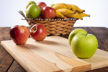fruit basket with bananas, apples and oranges on polished wood, placed on rustic wood with selective focus.