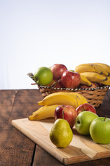 fruit basket with bananas, apples and oranges on polished wood, placed on rustic wood with selective focus.
