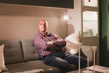 A carefree relaxed man dressed in a red plaid shirt and jeans is relaxing on a sofa in a cozy living room enjoying a lazy day off.
