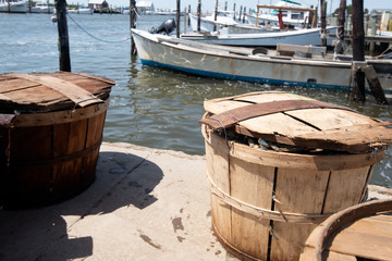 Bushel baskets full of blue crabs sit on a dock on the Chesapeake Bay with boats in the background.