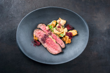 Modern style Commonwealth Sunday roast with sliced cold cuts roast beef, pickled mushrooms and vegetable chips offered as close-up on a cast-iron design plate