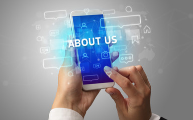 Female hand typing on smartphone with ABOUT US inscription, social media concept