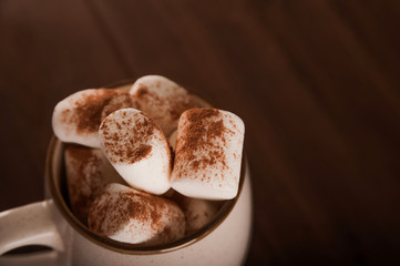 Marshmallows in a mug on a dark background close-up and copy space. Marshmallow in a cup with cocoa pattern top view in a dark key.