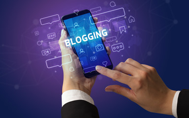 Female hand typing on smartphone with BLOGGING inscription, social media concept