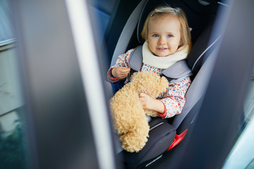 Adorable toddler girl in modern car seat with her favorite stuffed toy